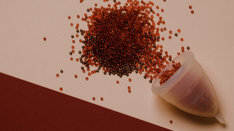 Red background with a menstrual cup spilling red beads to signify blood